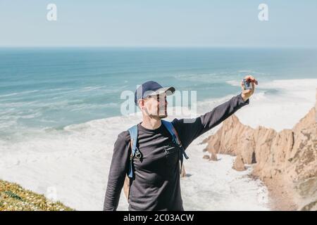 Ein Tourist fotografiert eine schöne Landschaft oder macht ein Selfie vor dem Hintergrund des Atlantischen Ozeans in Portugal. Stockfoto