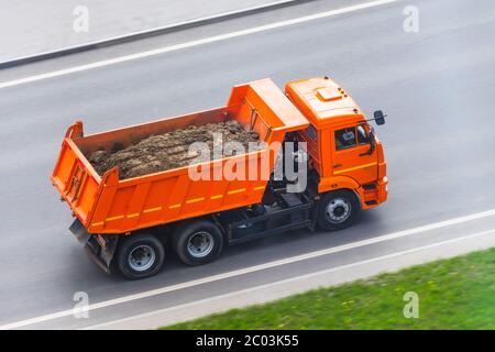 Orange LKW-Kippe mit einer Ladung Erde in der Karosserie fährt auf der Autobahn Stockfoto