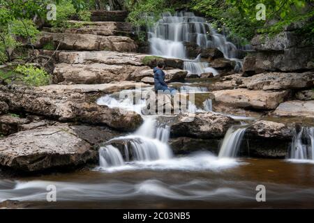 Frau auf Felsen beobachtet Lower East Gill Force, wo sie in die River Swale in der Nähe von Keld, Yorkshire Dales National Park, Großbritannien. Stockfoto