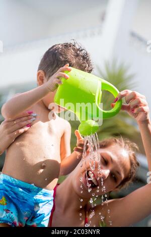 Vertikales Foto einer Frau und eines Kindes in einem Badeanzug Leeren einer farbigen Gießkanne während lächeln Stockfoto