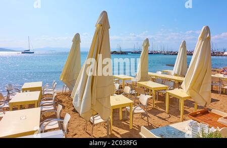 Open-Air-Café mit Tischen und Sonnenschirmen am Strand in Erwartung der Gäste an sonnigen Sommertag. Griechenland Stockfoto