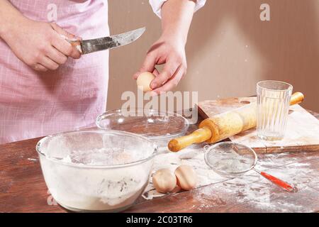 Vorbereitung des Tests für Pelmeni, Menschenhände brechen Ei über einer Tasse Stockfoto