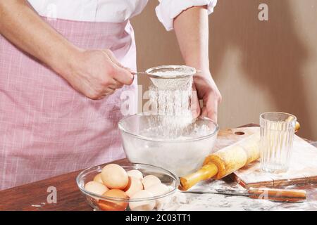 Vorbereitung des Tests für Pelmeni, Mann die Hand hält ein Sieb mit einem Mehl über eine Schüssel Stockfoto