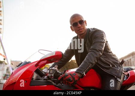 Schöner männlicher Biker in Lederjacke und Sonnenbrille, sitzt auf einem Motorrad, Platz kopieren Stockfoto