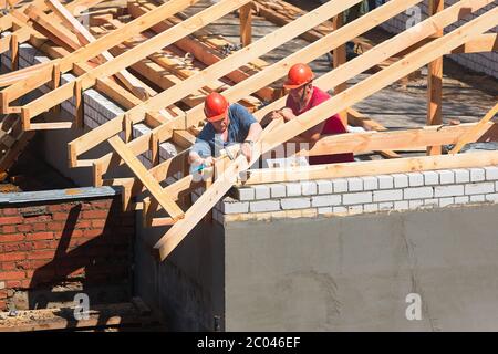 Zwei Arbeiter Dachdecker in Helmen von Dachsparren und Balken auf der Baustelle umgeben bauen Haus. Ein Paar Zimmerleute haben Holzdachkonstruktion aufgestellt Stockfoto