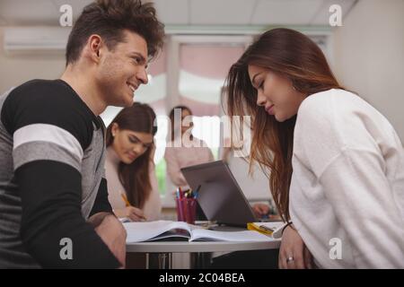 Liebe, dating, Teens Konzept. Low Angle Shot von einem gutaussehenden männlichen Kursteilnehmer Flirten mit seiner Freundin während der Klasse. Junge Hochschule Paar sprechen und Stockfoto