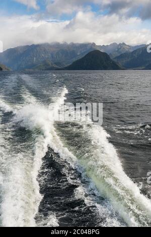 Die Folge eines Bootes, das schnell auf dem Lake Manapouri New Zealand mit den Bergen in der Landschaft im Hintergrund unterwegs ist. Stockfoto