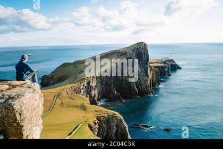 Touristen genießt auf dem Gipfel des Rock-Imperiums. Verträumte Landschaft, Frühling orange rosa Himmel. Neist Point und Leuchtturm an sonnigen Tagen in den schottischen Highlands, Großbritannien. Stockfoto