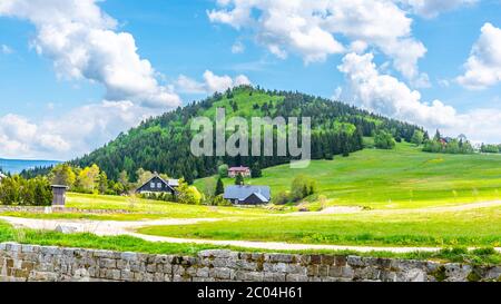 Bukovec Berg oberhalb des Dorfes Jizerka. Sommerlandschaft mit grünen Wiesen, blauem Himmel und weißen Wolken. Isergebirge, Tschechische Republik. Stockfoto