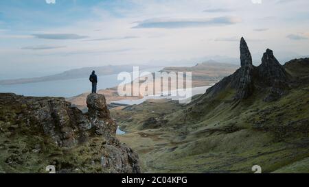 Junger Mann klettert bei Sonnenuntergang siegreich auf den Berg. Berühmte freiliegende Felsen Old man of Storr, Nordhügel auf der Insel Skye Stockfoto