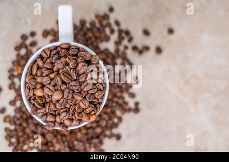Eine weiße Tasse gefüllt mit gerösteten Zimt Kaffeebohnen stehen auf braunem Marmor von Kaffeebohnen umgeben Stockfoto