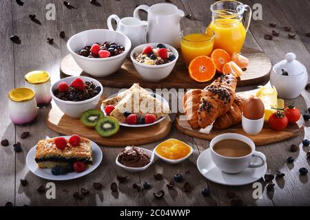 Das Frühstück wird mit Kaffee, Orangensaft, Croissants, Pfannkuchen, Ei, Müsli und Obst serviert. Stockfoto