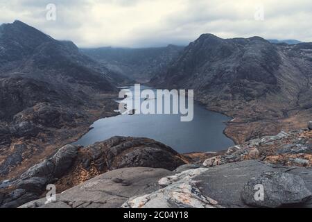 Panoramablick auf eine hügelige Landschaft mit See während eines Tages. In der Nähe von Loch Coruisk liegt ein Binnengewässer, der am Fuße des Black Cuil liegt Stockfoto