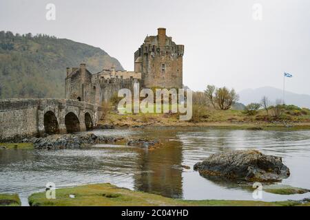 Blumen vor dem prächtigen Eilean Donan Castle, Schottland. Die beliebte steinerne Brücke über Wasser mit massiven Wasserbüschel Stockfoto