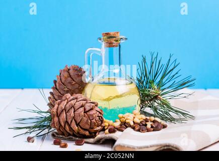 Zusammensetzung, Zedernöl mit Zapfen und Nüssen auf einem weißen Holztisch auf blauem Hintergrund Stockfoto