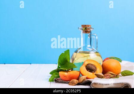 Zusammensetzung, Flasche mit Aprikosenöl und Samen auf einem weißen Holztisch auf blauem Hintergrund Stockfoto