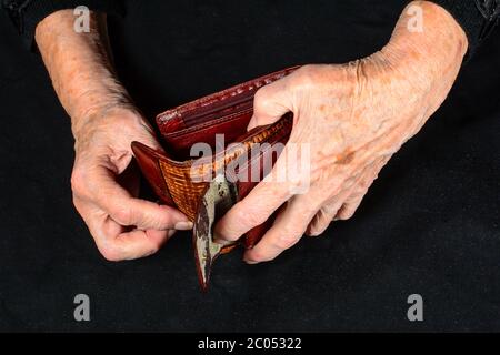 Hände der alten Frau, die versucht, wenig Geld in alten schäbigen Brieftasche zu finden. Das Konzept des Mangels an Geld im Alter und kleine Renten. Nahaufnahme in einer Dunkelheit Stockfoto