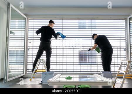 Horizontale Ansicht von zwei männlichen professionellen Reinigern Reinigung Jalousien auf einer großen Fensterfront mit Mikrofasertüchern Stockfoto