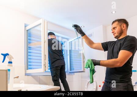 Ein Blick auf zwei professionelle Reinigungskräfte in einem modernen Bad Reinigung der Schränke und Spiegel und Jalousien Stockfoto