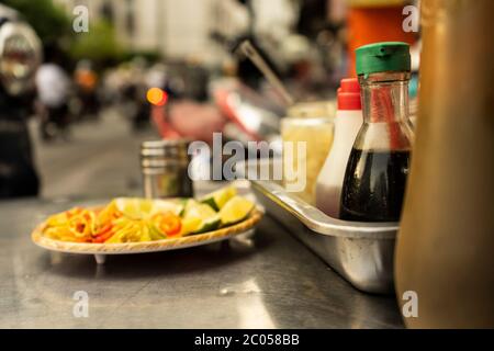 Traditionelle vietnamesische Nudelwürztablett mit Gericht aus Zitronenscheiben, Glas Chili, Fischsauce, Sojasauce, Löffel und Essstäbchen auf der Straße Food-Cart Stockfoto