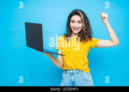 Emotionale junge Frau mit Laptop feiert Sieg auf farbigen Hintergrund Stockfoto