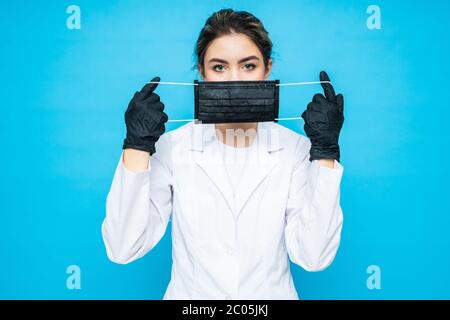 Junge Frau in einem chirurgischen Anzug, trägt eine Schutzmaske auf ihrem Gesicht und Handschuhe auf den Händen posiert, während vor einem blauen Hintergrund stehen. Schutz. Ca Stockfoto