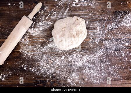 Brotteig neben einem Nudelholz auf einem Holztisch voller Mehl, Konzept der gesunden hausgemachten Speisen Stockfoto