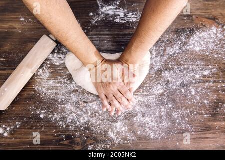 Hände einer nicht erkennbaren Person, die Brotteig auf einem Holztisch knetet, Konzept der gesunden Ernährung zu Hause Stockfoto