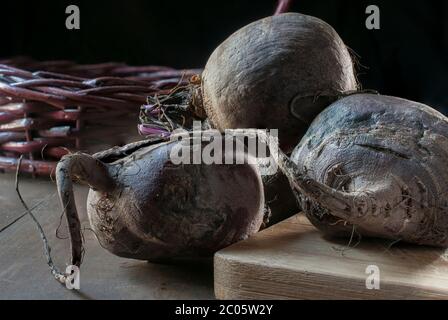 Rote Bete auf einem Holzschneidebrett und einem Korb unten mit schwarzem Hintergrund und einem Rand Licht, Konzept von Bio-Gemüse auf einem Tisch Stockfoto