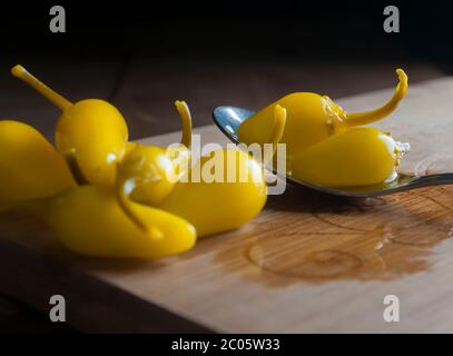Pepperoncini Paprika auf einem Löffel und auf einem hölzernen Schneidebrett Makro-Fotografie oder Nahaufnahme Bild, in einem dunklen Hintergrund würzige Lebensmittel-Konzept Stockfoto