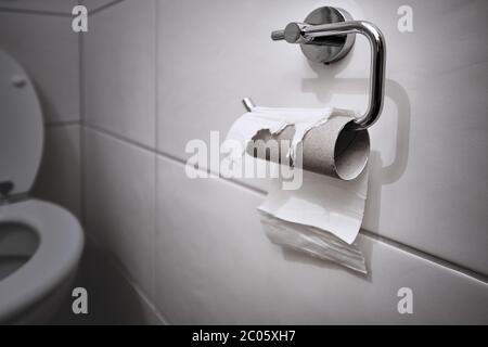 Nicht auf Lager, kein Toilettenpapier mehr. Letztes Stück Papier auf einer Rolle in einem sauberen und leeren weißen Badezimmer. Panik, Angst und weltweite Einkaufskrise. Stockfoto