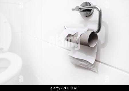 Nicht auf Lager, kein Toilettenpapier mehr. Letztes Stück Papier auf einer Rolle in einem sauberen und leeren weißen Badezimmer. Panik, Angst und weltweite Einkaufskrise. Stockfoto