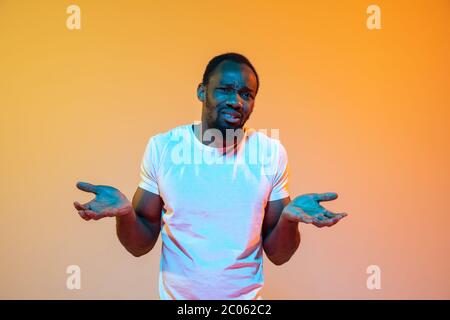 Unsicher, fühlt sich schuldig, wtf. afroamerikanischer Mann modernes Porträt auf gradient orange Studio Hintergrund in Neon. Schönes Afro-Modell. Konzept der menschlichen Emotionen, Gesichtsausdruck, Verkauf, Anzeige. Stockfoto