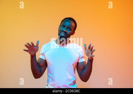 Unsicher, fühlt sich schuldig, wtf. afroamerikanischer Mann modernes Porträt auf gradient orange Studio Hintergrund in Neon. Schönes Afro-Modell. Konzept der menschlichen Emotionen, Gesichtsausdruck, Verkauf, Anzeige. Stockfoto