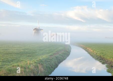 Windmühle im Morgennebel am Fluss Stockfoto