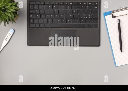 Flacher Schreibtisch mit Blick von oben. Arbeitsplatz mit leerem Clipboard, Laptop, Notizblock, Stift, Thermometer. Medizinisches Konzept Stockfoto