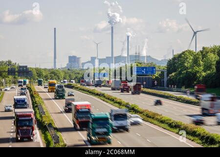 Viele Lkw fahren auf der Autobahn A2, hinten das Kohlekraftwerk Uniper Gelsenkirchen Scholven, rechts eine Windkraftanlage, Industrie Stockfoto