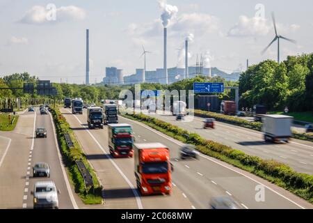 Viele Lkw fahren auf der Autobahn A2, hinten das Kohlekraftwerk Uniper Gelsenkirchen Scholven, rechts eine Windkraftanlage, Industrie Stockfoto