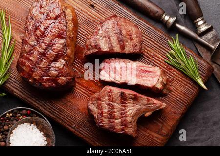Gegrillte Rindersteaks mit Gewürzen und Kräutern auf Schneidebrett. Draufsicht flach liegend Stockfoto