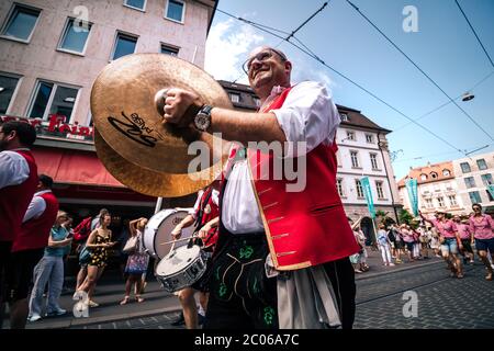 Rot gekleideter Messingmusiker mit riesigen Handbellen in typischer Volkskostüme aus dem Dorf Püssensheim bei der Eröffnungspartade des Kiliani Sommerfair. Stockfoto