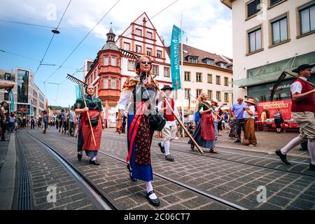 Menschen präsentieren die bunte traditionelle Kleidung und tragen typische Erntewerkzeuge bei der Kiliani Sommer Festival Eröffnungsparade in Bayern. Stockfoto