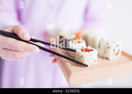 Nahaufnahme einer Frau, die Sushi-Set und Essstäbchen mit Holzplatte hält. Stockfoto
