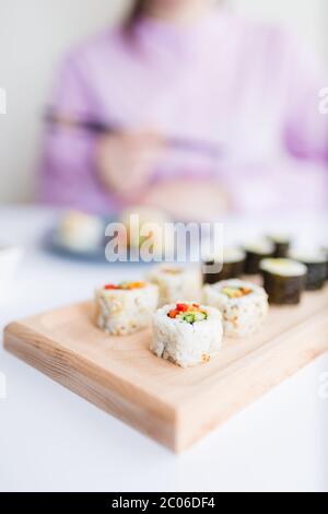 Nahaufnahme der Sushi-Portion auf dem Tisch mit weiblichen Stäbchen im Hintergrund. Stockfoto