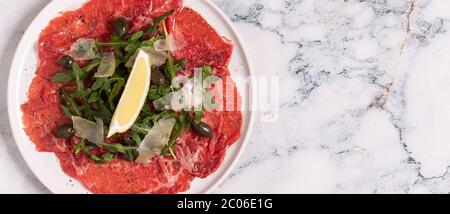 Marmorierte Rind-Carpaccio mit Rucola, Kapern, Zitrone und Parmesan, Draufsicht Stockfoto