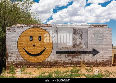 Smiley-Gesicht und Pfeil auf der Seite eines alten Backsteingebäudes auf dem Highway 54, alte Route 66 in Vaughn, New Mexico Stockfoto