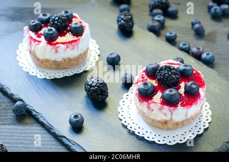 Köstlicher Erdbeerkäse auf schwarzem Teller mit frischen Blaubeeren im Hintergrund Stockfoto