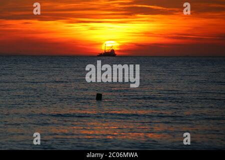 Sonnenuntergang über dem Meer. Ein kommerzielles Fischerboot vom Typ Drifter (Trawler), das vor der Sonne vorbeifährt und auf dem Weg zum Nachtfischen ist. Wolken bedecken die Stockfoto