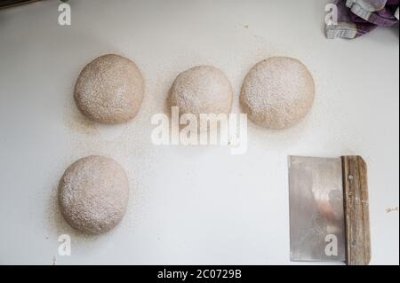 Draufsicht auf vier rohe Sauerteig-Brötchen, die mit Dinkelmehl auf der Küchentheke bestäubt wurden. Stockfoto