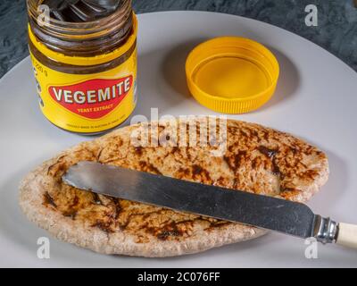 Ein Glas neu geöffneten Vegetmit Hefeextrakt, mit einigen auf einem gebutterten Vollkornbrot Pitta Brot auf einem Teller, mit einem Messer auf der Oberseite verteilt. Stockfoto