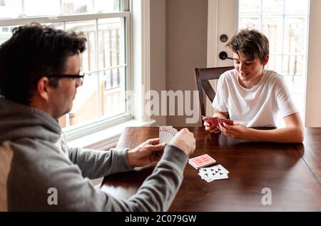 Der junge Mann und sein Vater spielen zusammen am Tisch Karten. Stockfoto